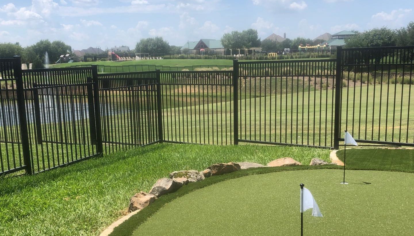 Metal fence enclosing a back lawn with a putting green